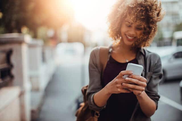 Young woman using smartphone, walking outdoors, smiling.
